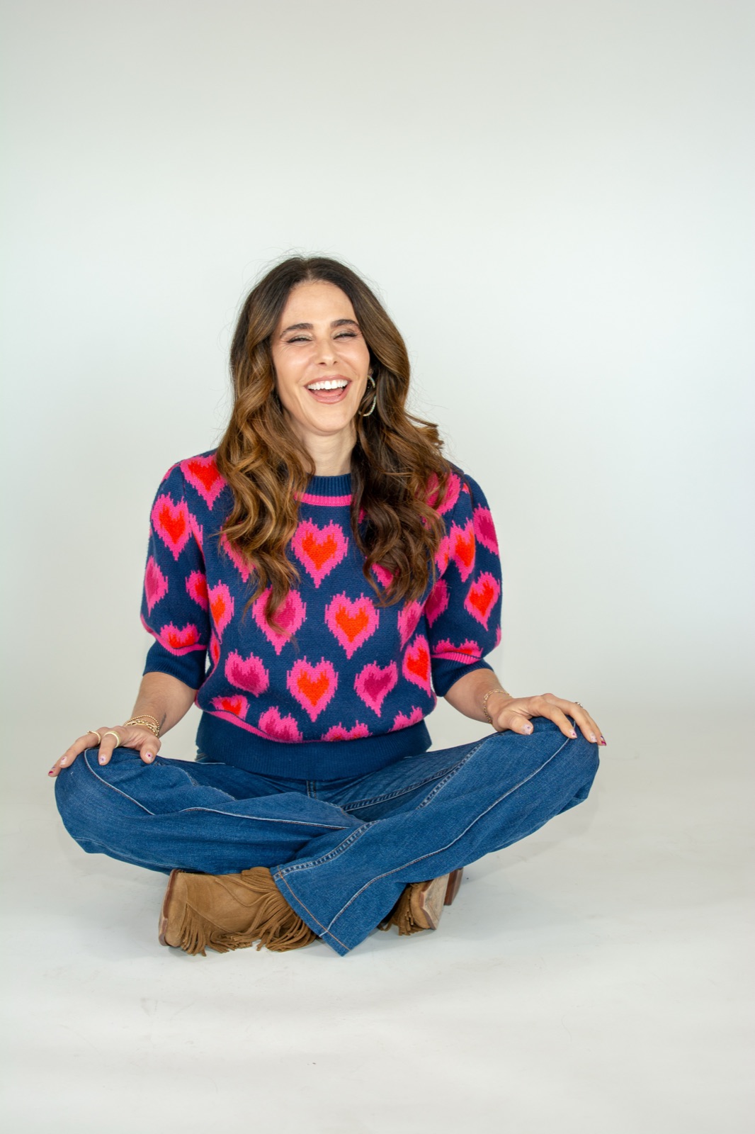 Cassie Blakely laughing, seated in a navy heart-print sweater